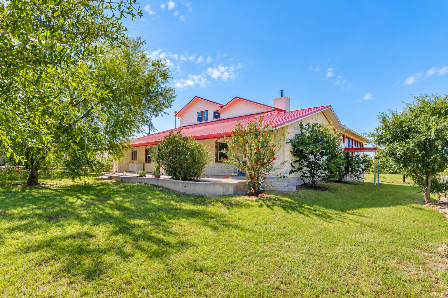 Real home exterior with a red metal roof, open concrete patio and green lawn from the agency catalog